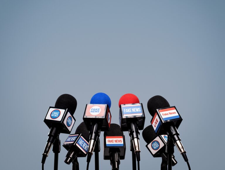 Microphones prepared for the press conference and mic flags displaying fake news logos: disinformation and propaganda concept, blank copy space